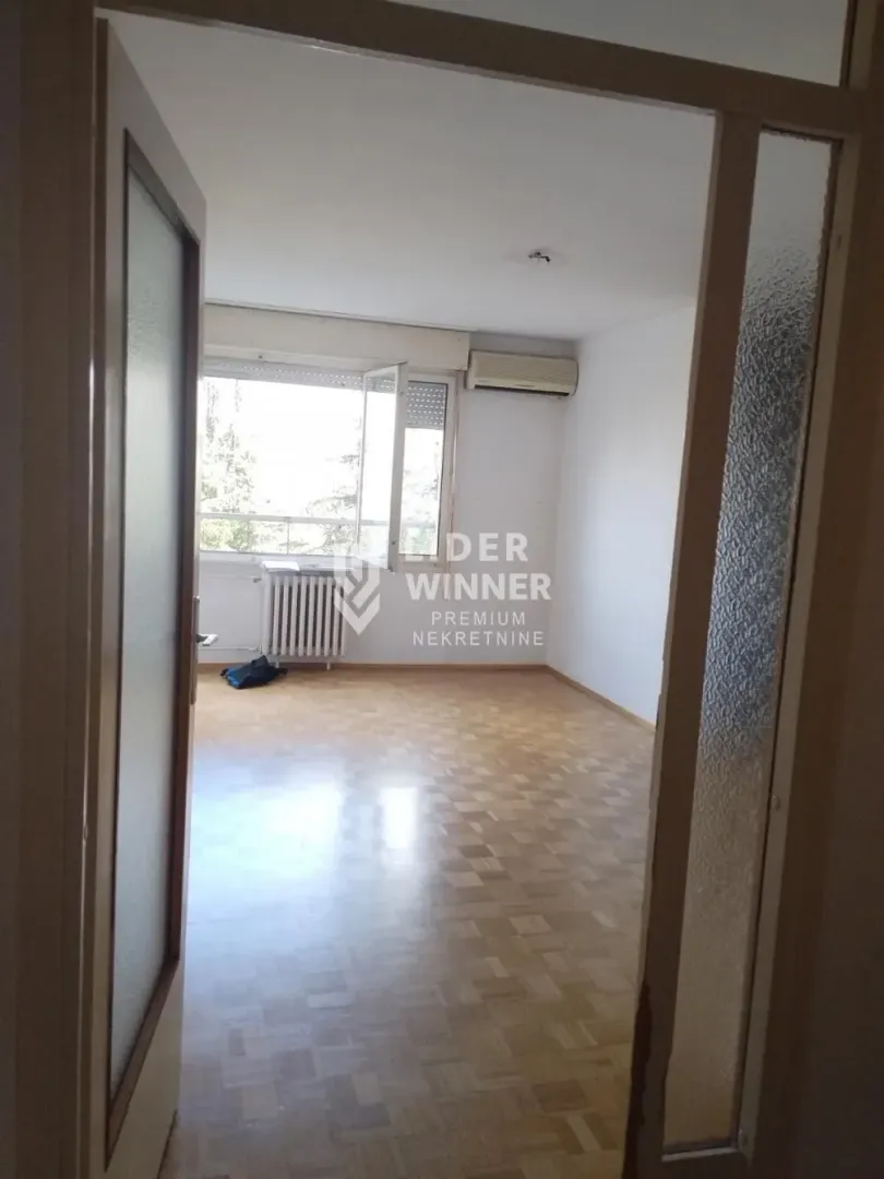 View from the hallway into an empty room with parquet flooring and an air conditioning unit.