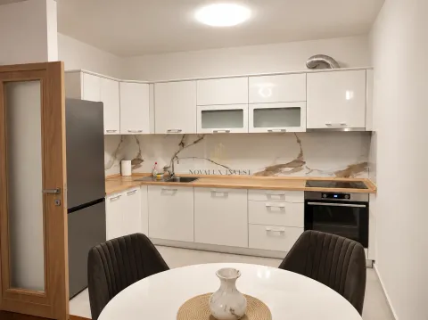 Moderna kuhinja sa bijelim elementima, ugradnim aparatima i trpezarijskim stolom u prvom planu. - image 3