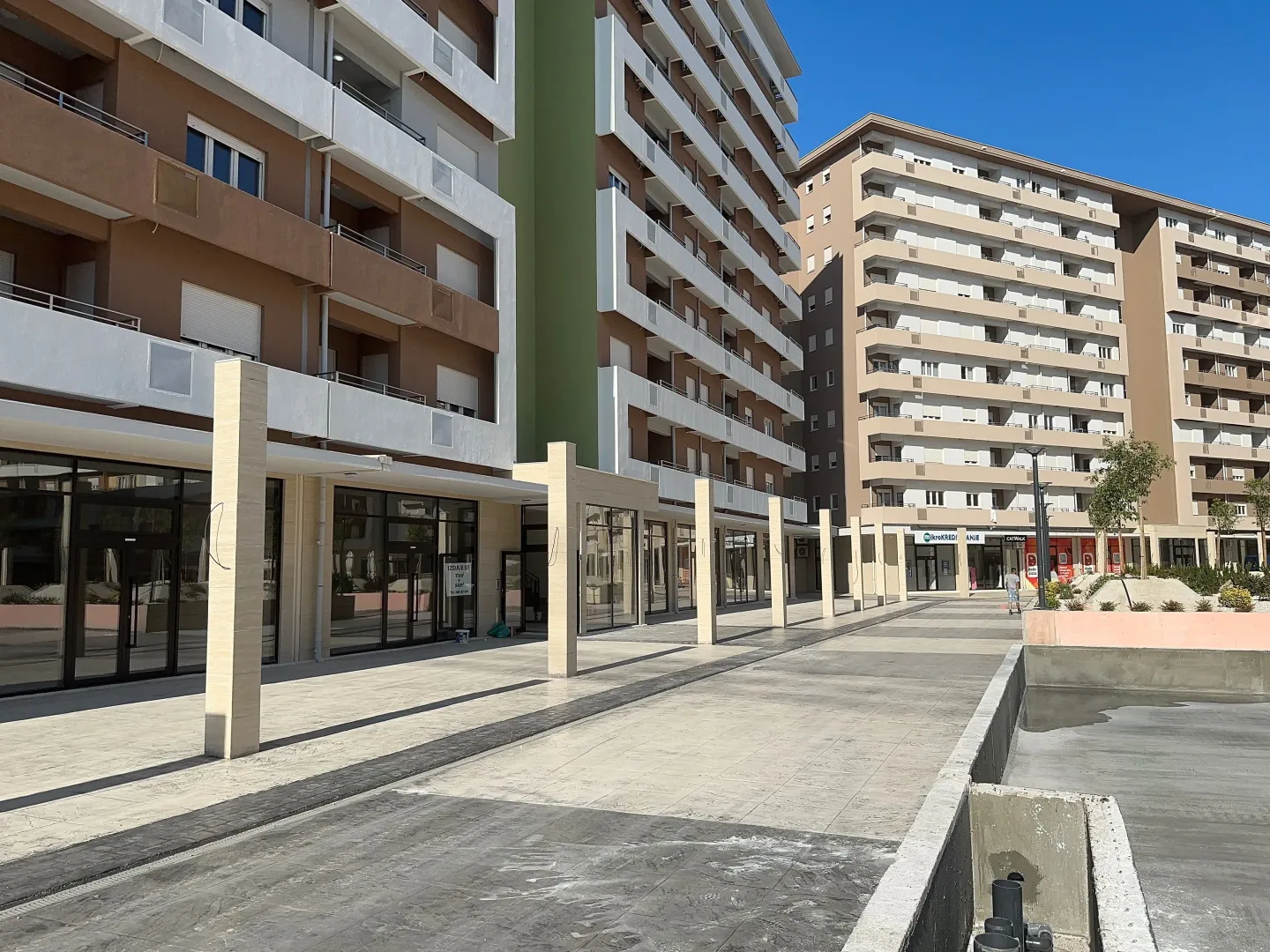 Eksterijer moderne stambene zgrade sa poslovnim prostorima u prizemlju i popločanim platoom.