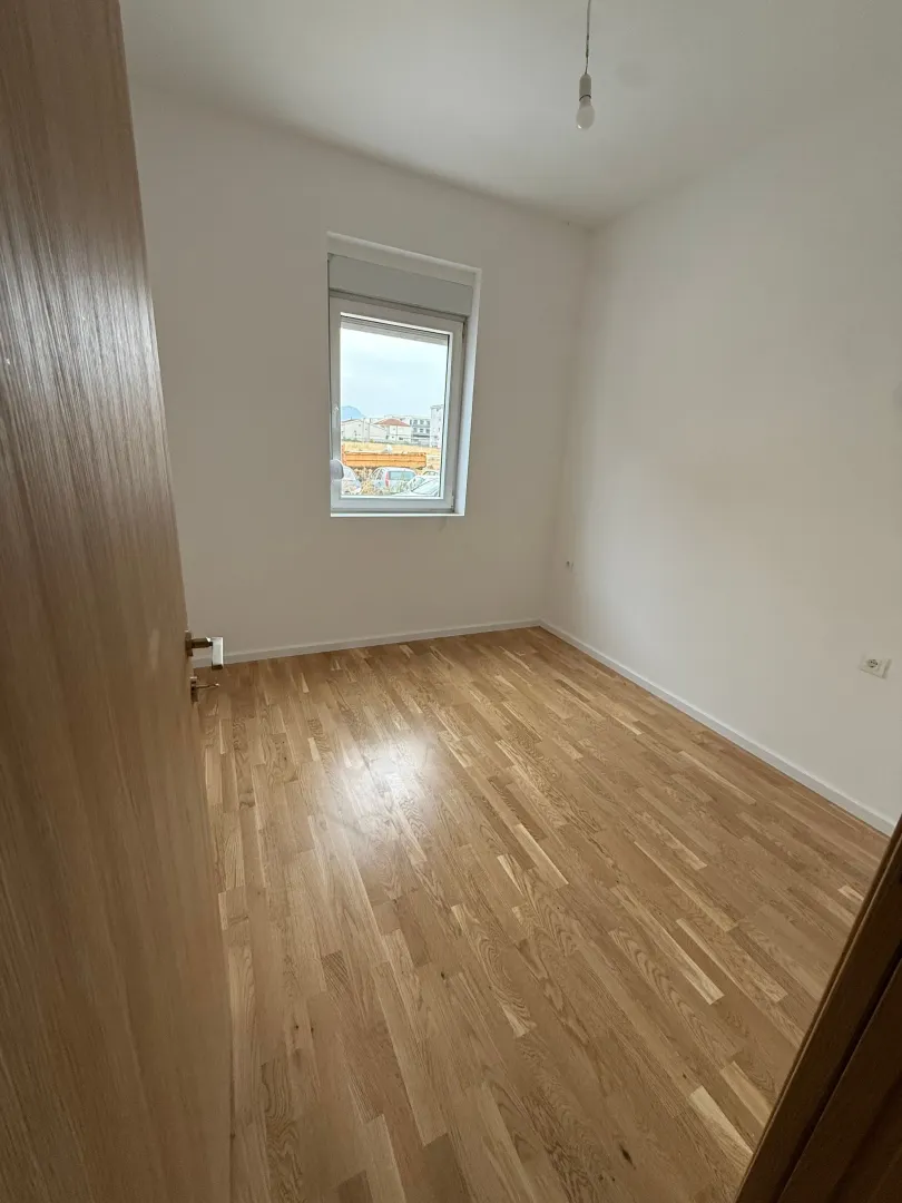 Prazna soba sa parketom i prozorom.