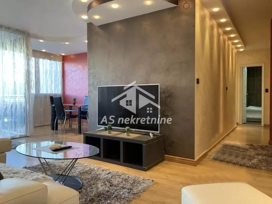 Dnevna soba sa televizorom, garniturom i trpezarijom u pozadini.