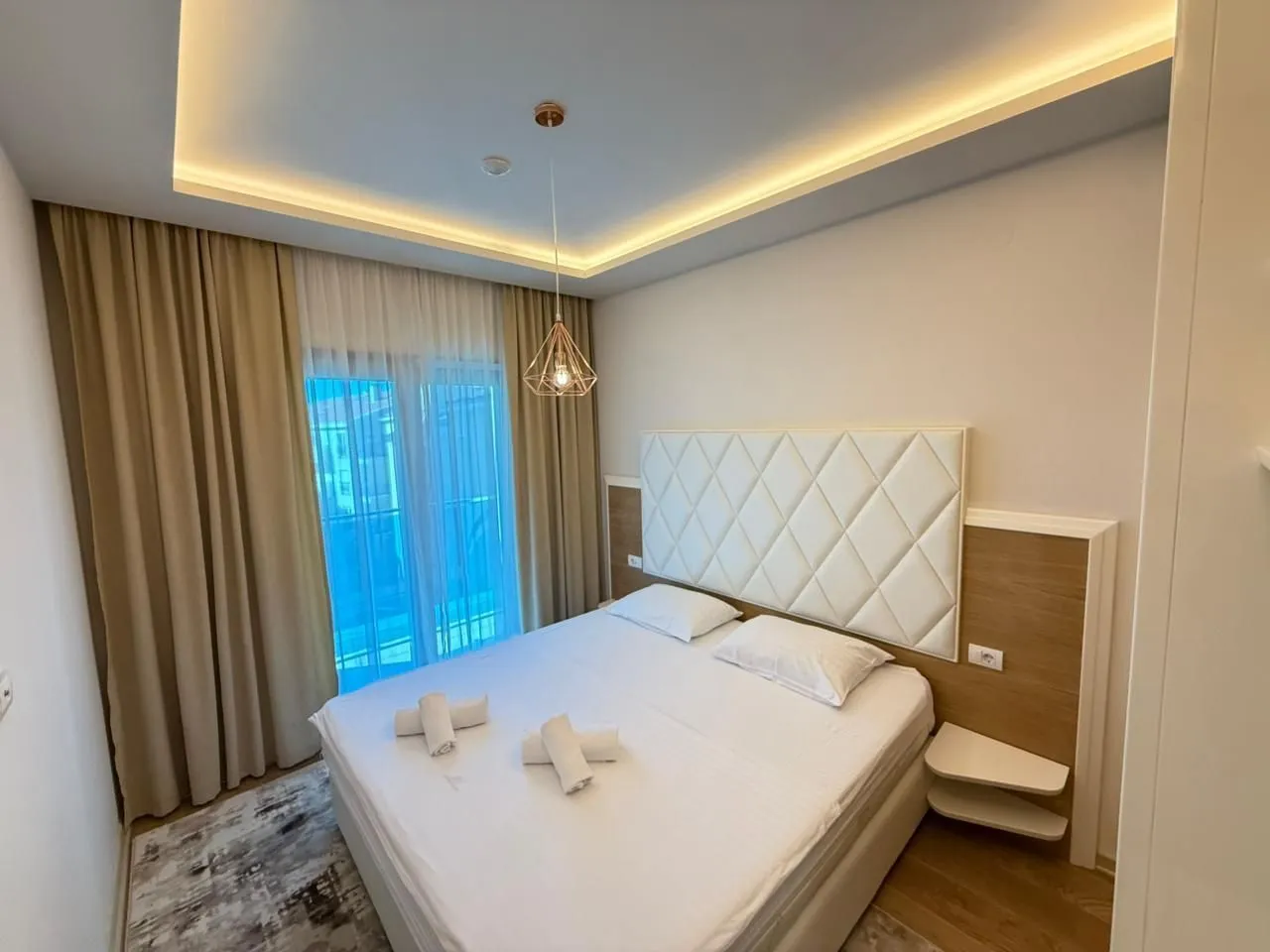 Modern bedroom with a double bed, upholstered headboard, and balcony access.