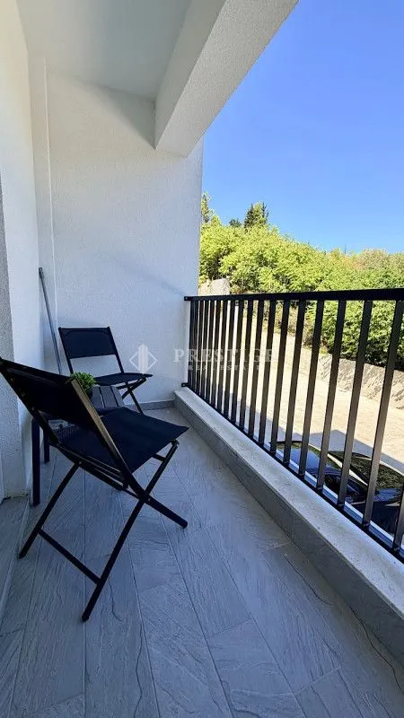 Natkrivena terasa sa crnim stolicama i pogledom na zelenilo.
