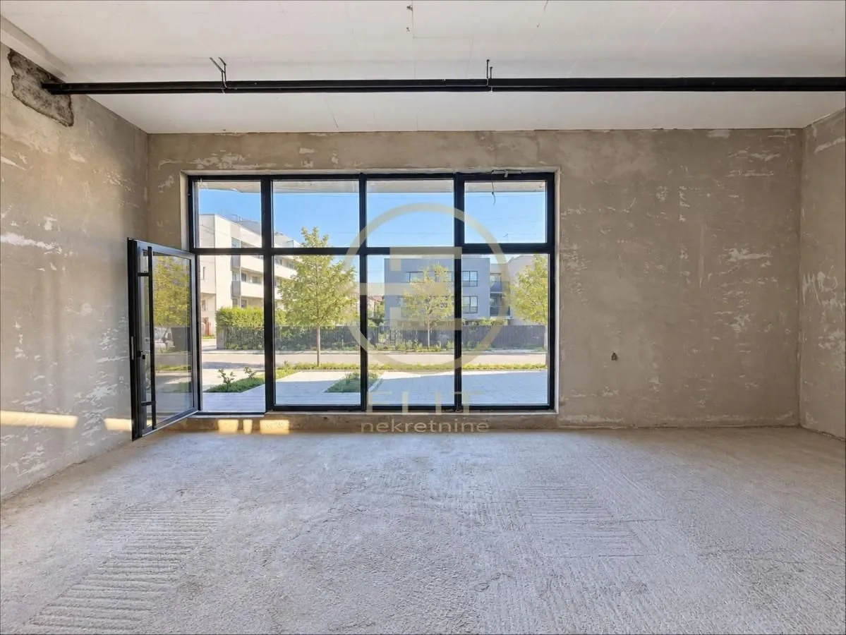 Unfinished room in grey phase with large glass windows and view of the courtyard.