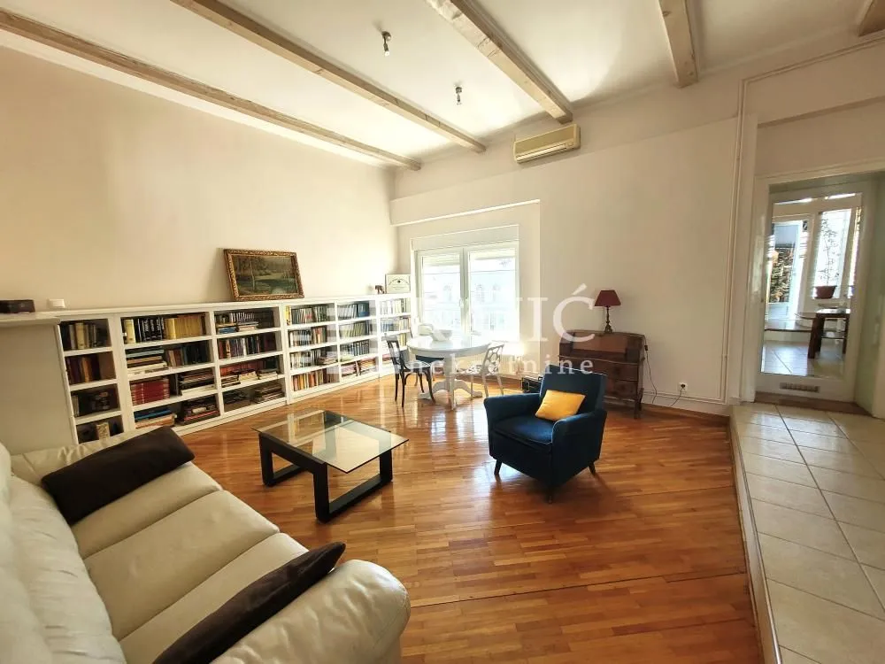 Spacious living room with wooden flooring, sofa set, and a large bookcase.