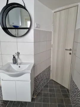 Small bathroom with a washbasin, round mirror, and tiling. - image 5