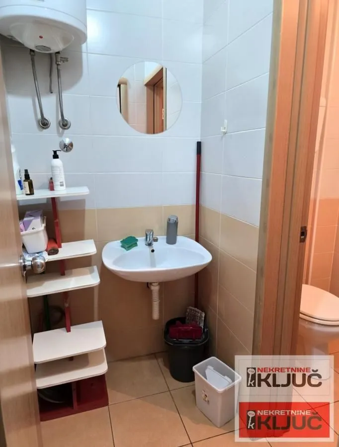 Smaller bathroom with a washbasin, water heater, and wall tiles.