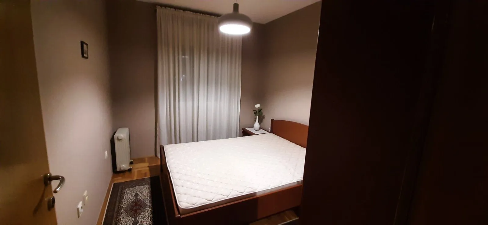 Spavaća soba sa bračnim krevetom i prozorom sa bijelim zavjesama.