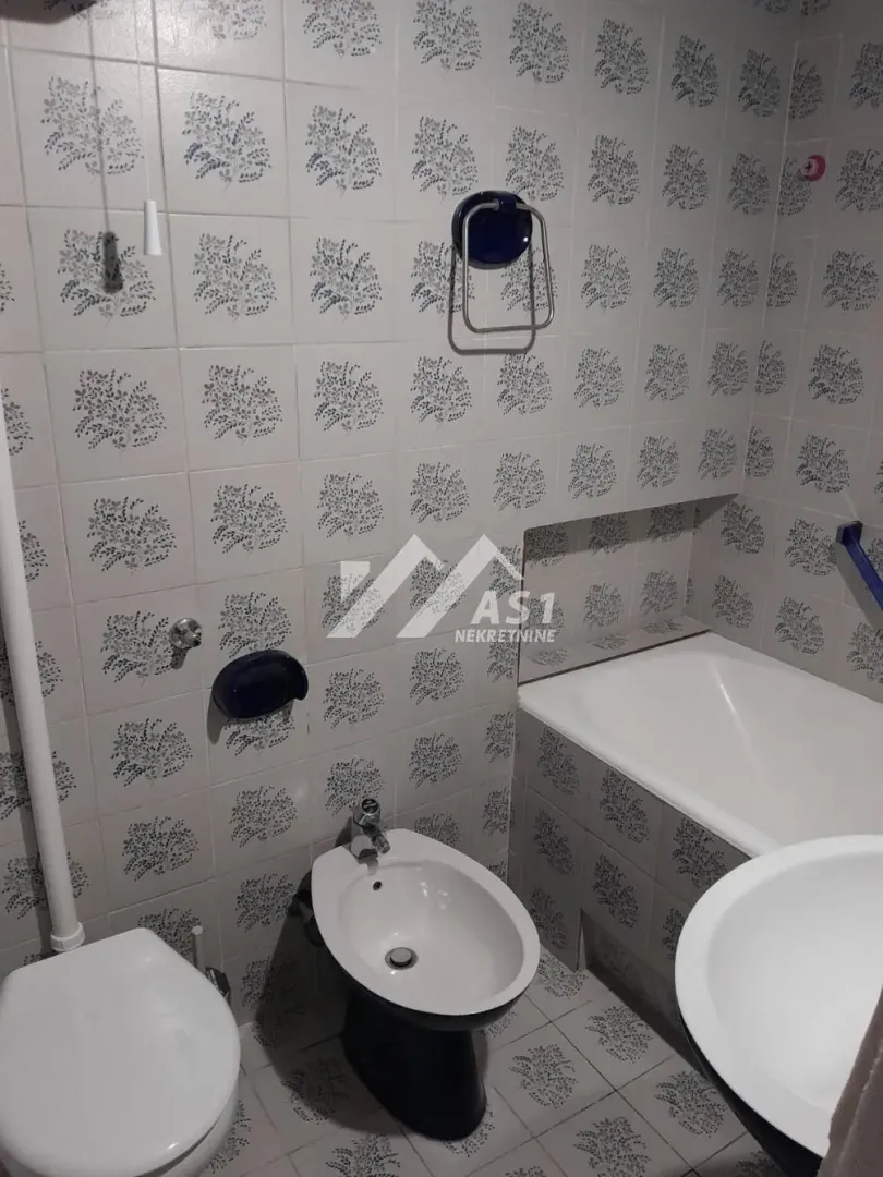 Kupatilo opremljeno sanitarijama, kadom i zidnim pločicama sa dezenom.