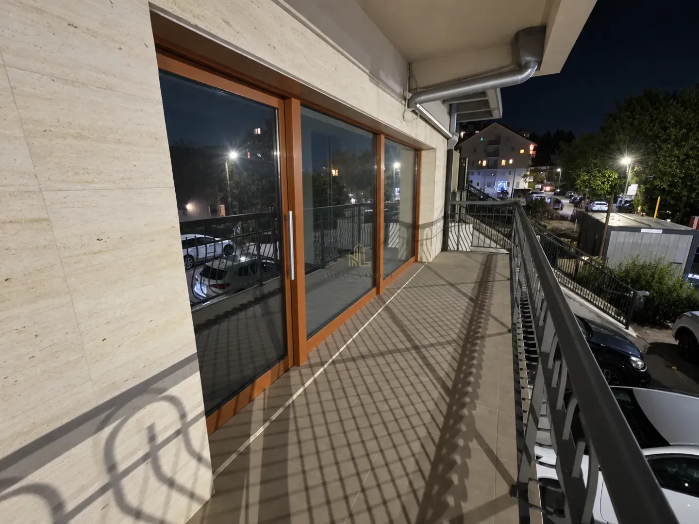 Spacious covered balcony with a metal railing and a view of the street at night.