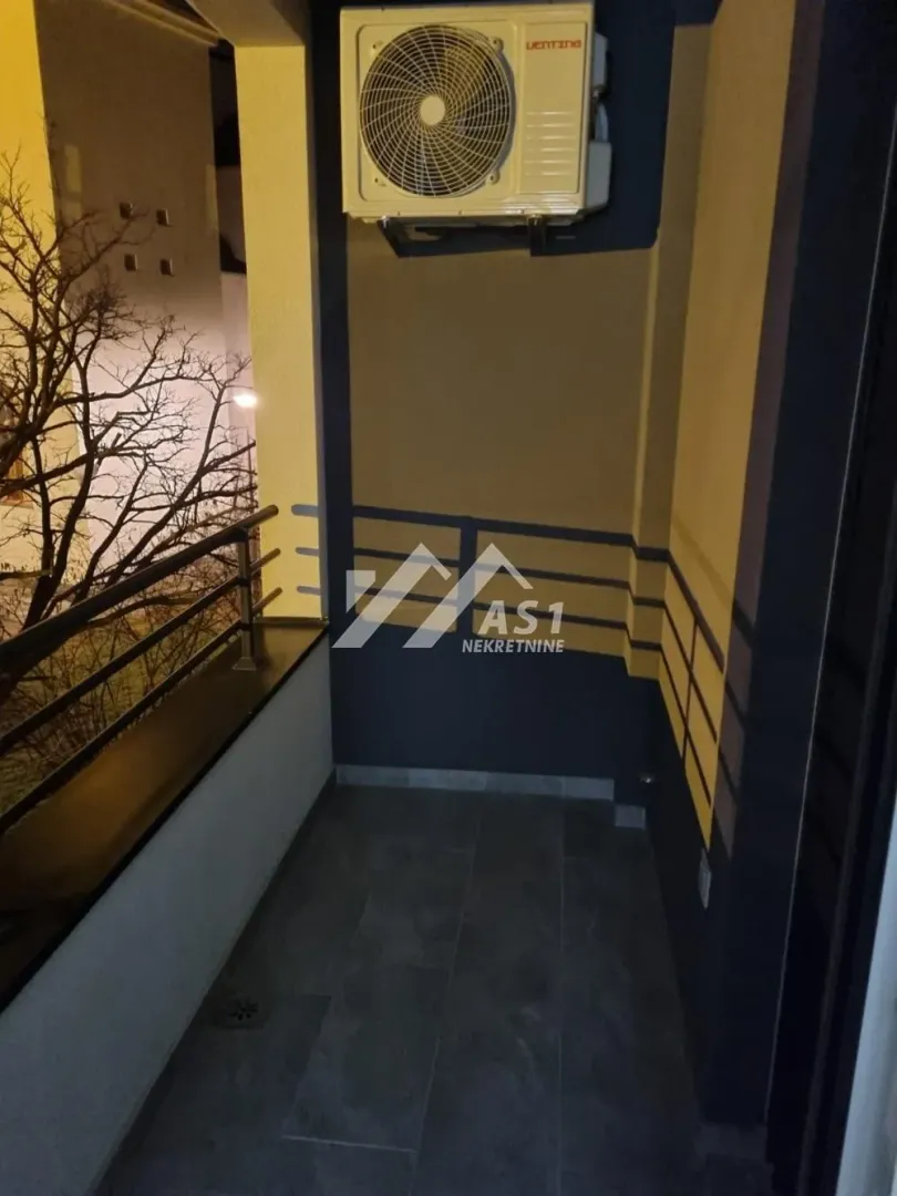 Natkriveni balkon sa spoljnom jedinicom klima uređaja i metalnom ogradom.