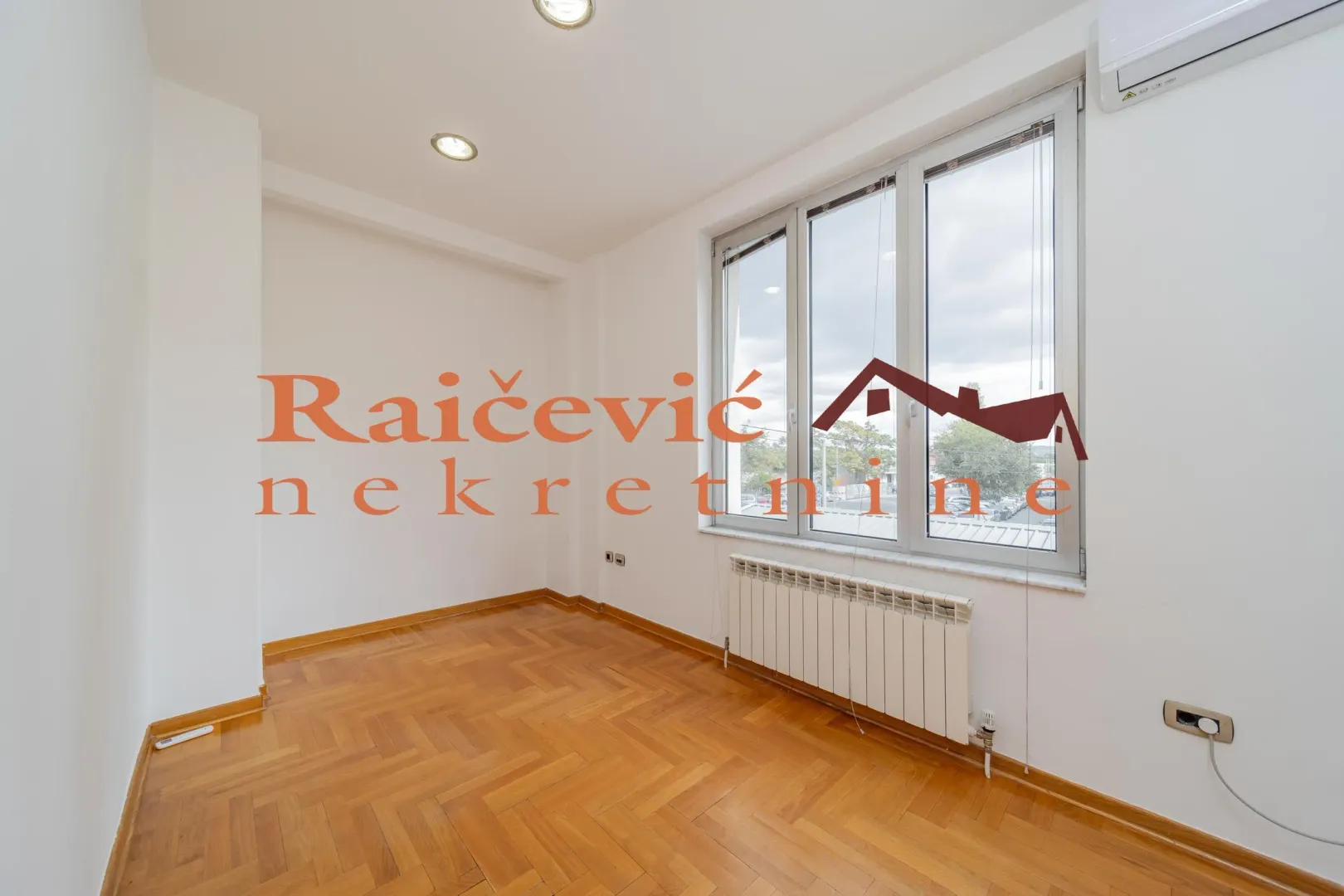 Empty room with parquet flooring and a large window.