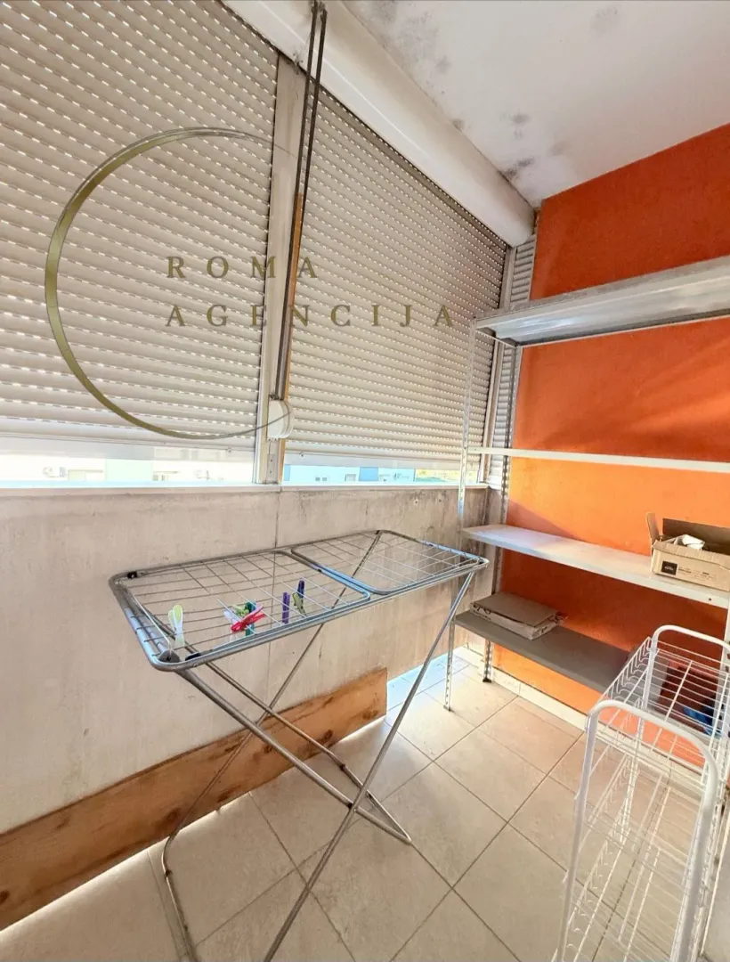 Enclosed balcony with a clothes drying rack and metal shelving units.