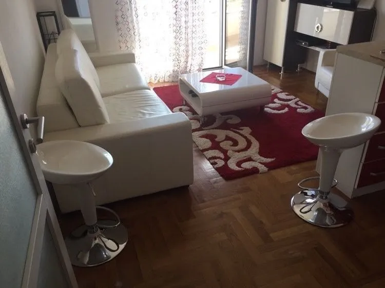 Living room featuring a white leather sofa, a red patterned rug, and bar stools.