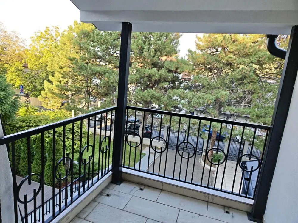 Natkriveni balkon sa crnom ogradom i pogledom na zelenilo i dvorište.