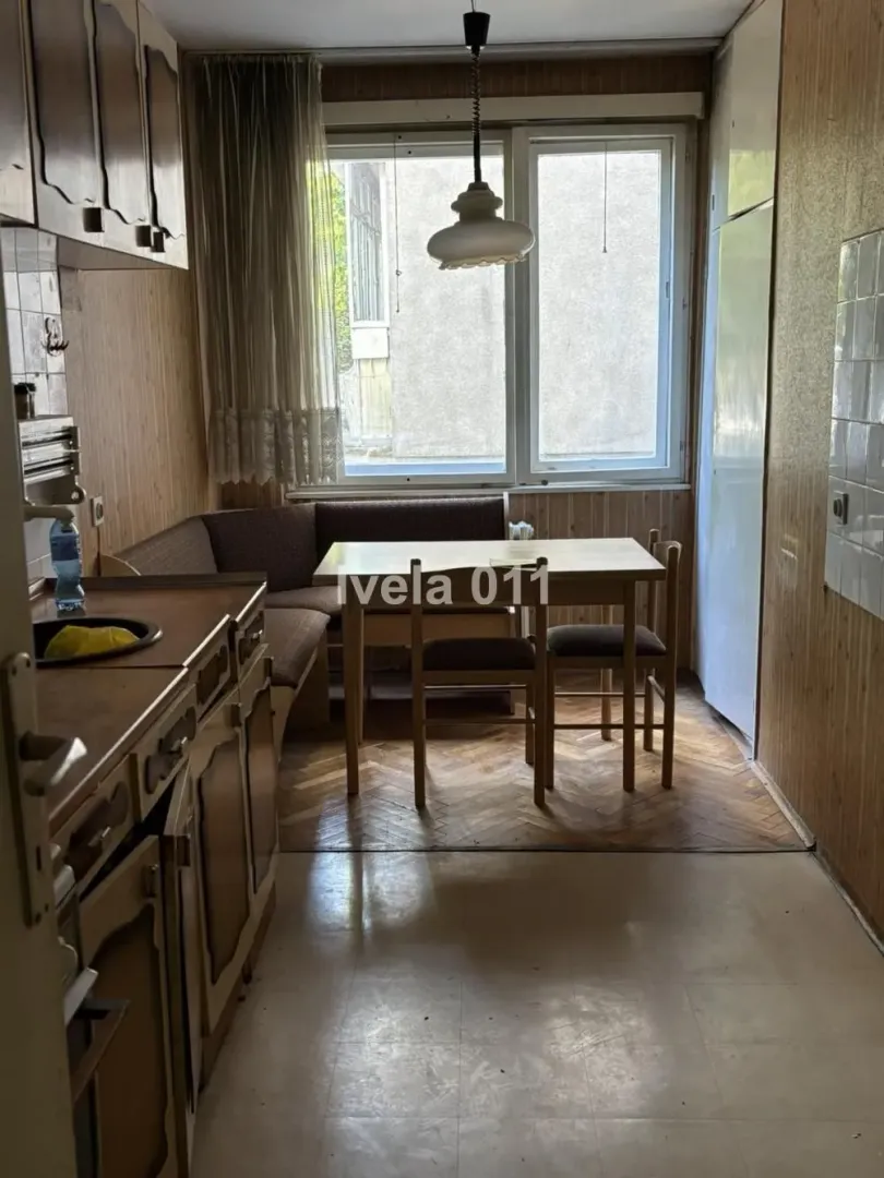 Starija kuhinja sa trpezarijskim stolom i ugaonom garniturom pored prozora.