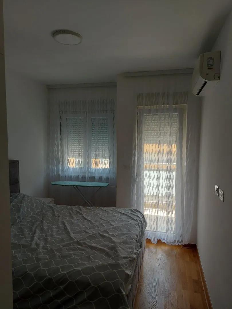 Spavaća soba sa bračnim krevetom, klima uređajem i prozorom sa zavjesama.