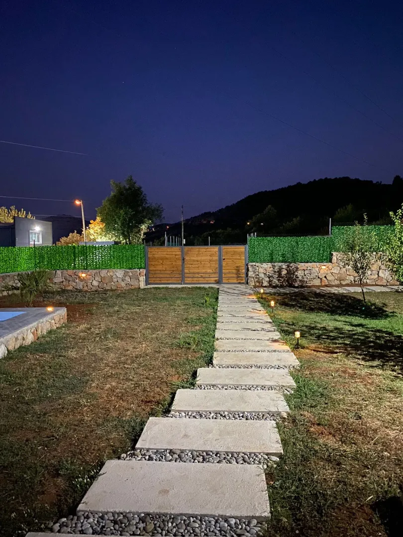 Illuminated yard with a paved walkway and a wooden gate at dusk.