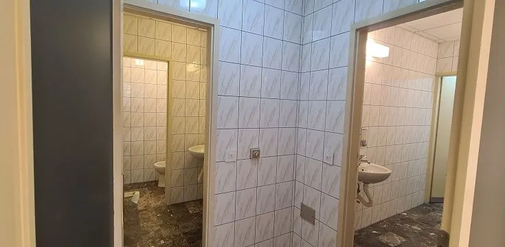 A view of a tiled bathroom with a washbasin and a doorway leading to a toilet.