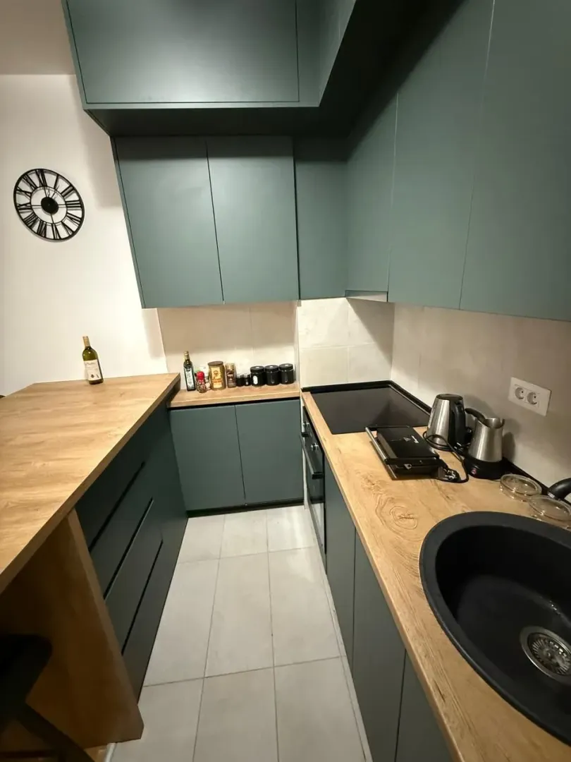 Modern kitchen with green cabinets and a wooden countertop.