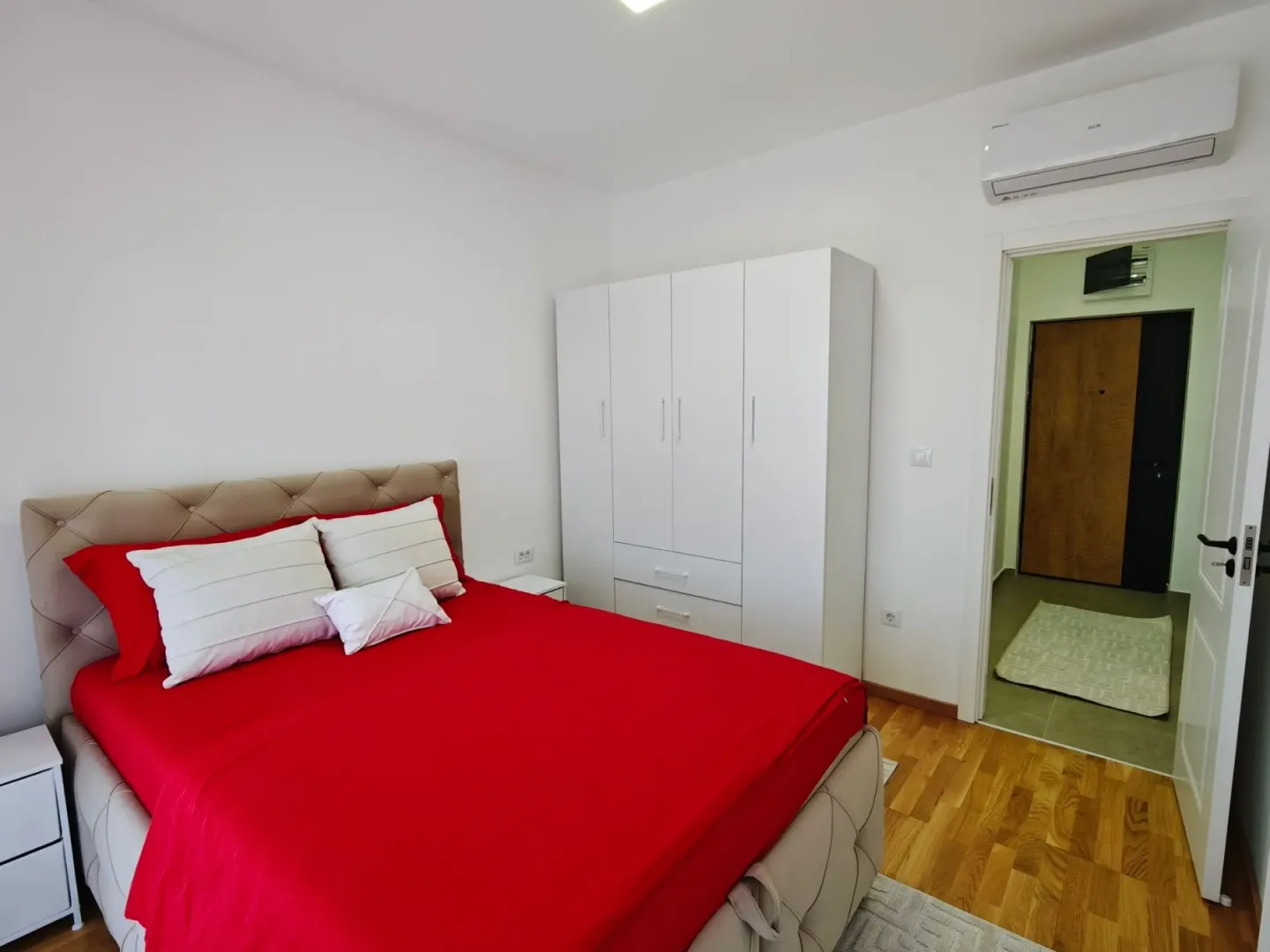 Bright bedroom with a double bed, white wardrobe, and air conditioning.