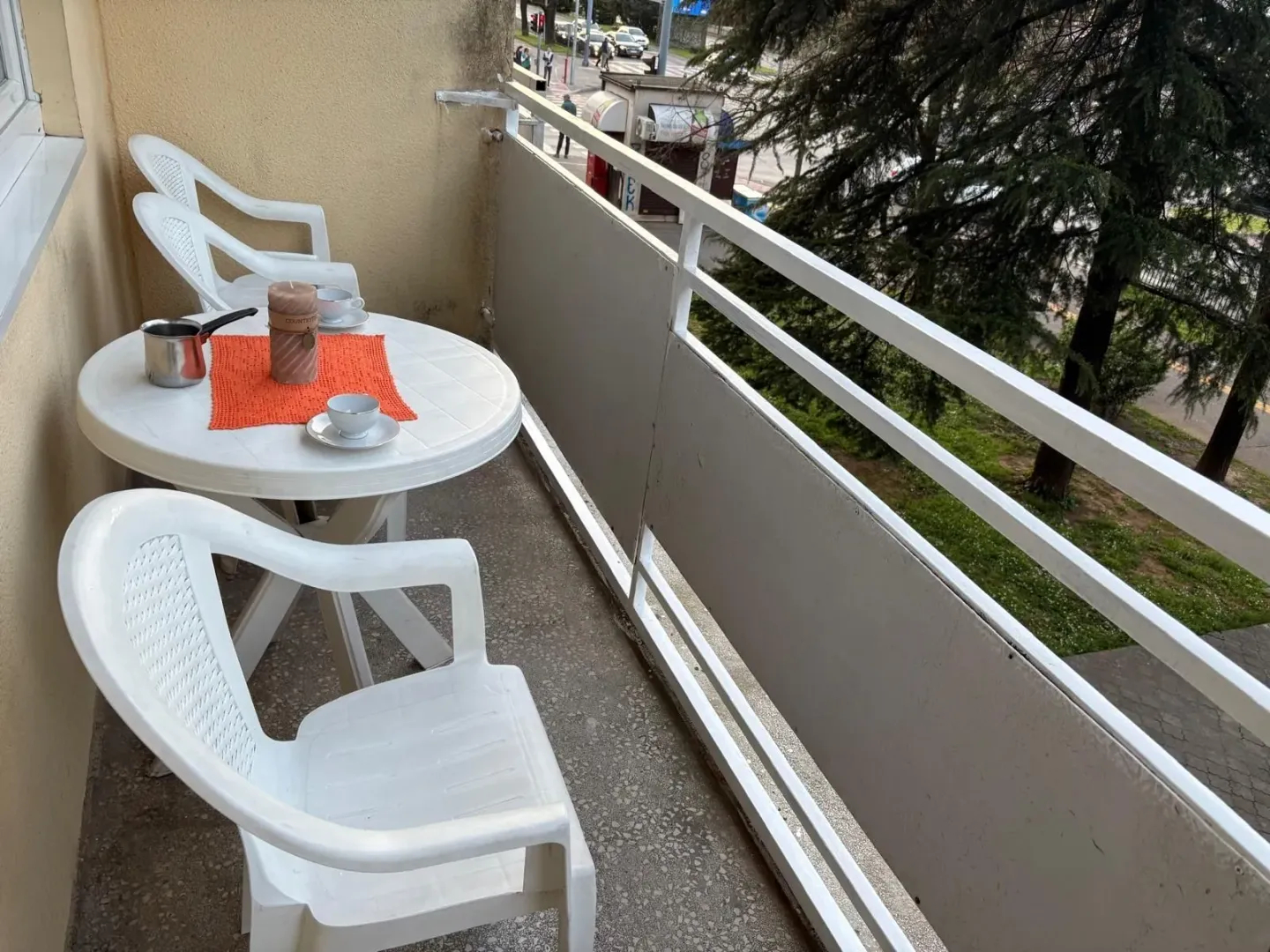 Balcony with a table, chairs, and a view of the street and trees.