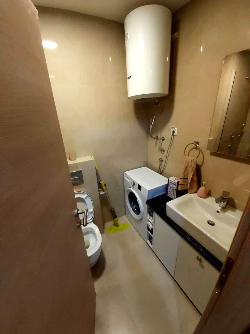 A small bathroom with a washing machine, water heater, sink, and toilet.