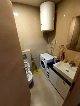 A small bathroom with a washing machine, water heater, sink, and toilet. - image 5