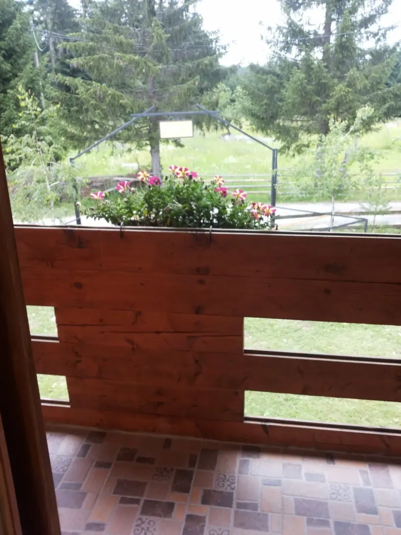 Pogled sa balkona sa drvenom ogradom i cvijećem prema dvorištu.