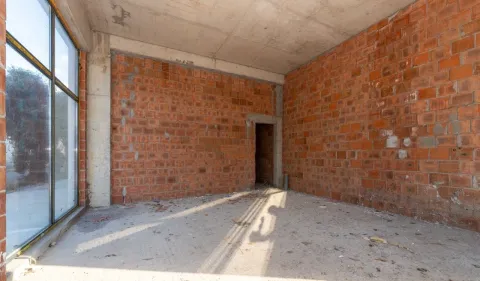 Unfinished room in grey phase with large windows and brick walls. - image 2