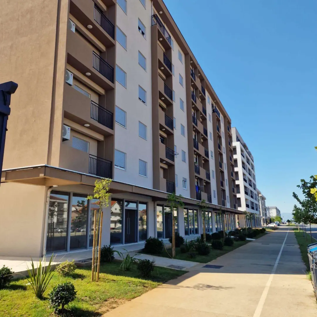 Exterior of a residential building with ground floor commercial spaces and a sidewalk.