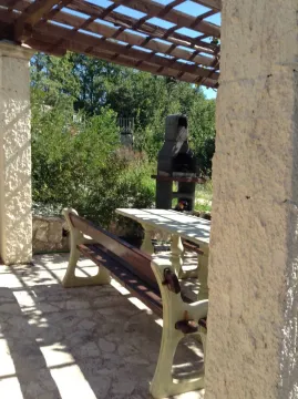 Popločano dvorište sa stolom, klupom i kamenim roštiljem ispod drvene pergole. - image 4