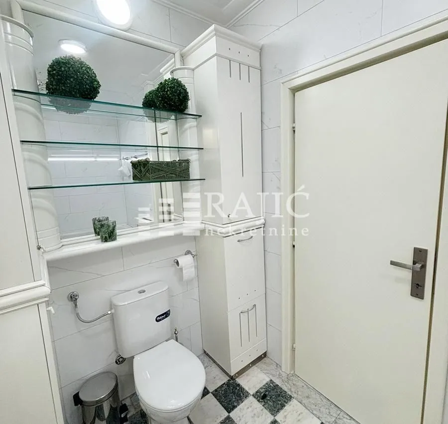 Smaller bathroom with white furniture, toilet, and a mirror with glass shelves.