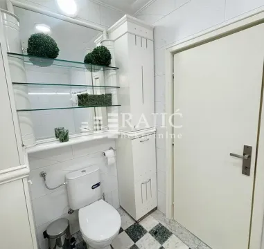 Smaller bathroom with white furniture, toilet, and a mirror with glass shelves. - image 12