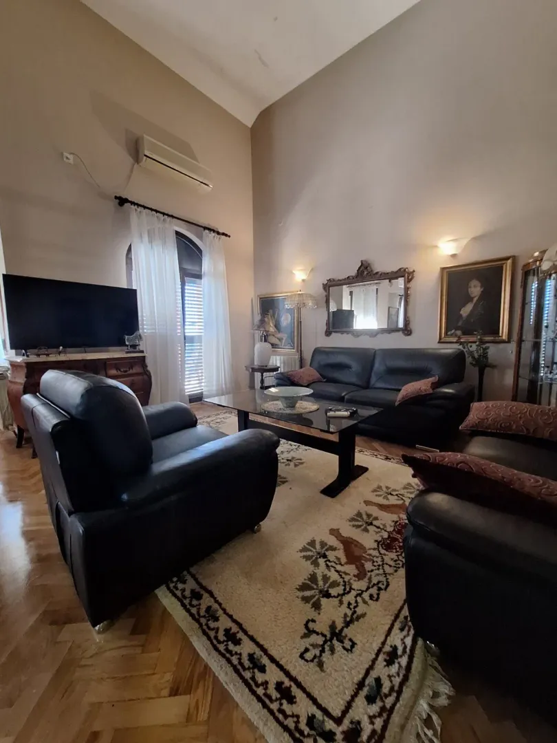 Spacious living room with black leather furniture, a rug, and a high ceiling.