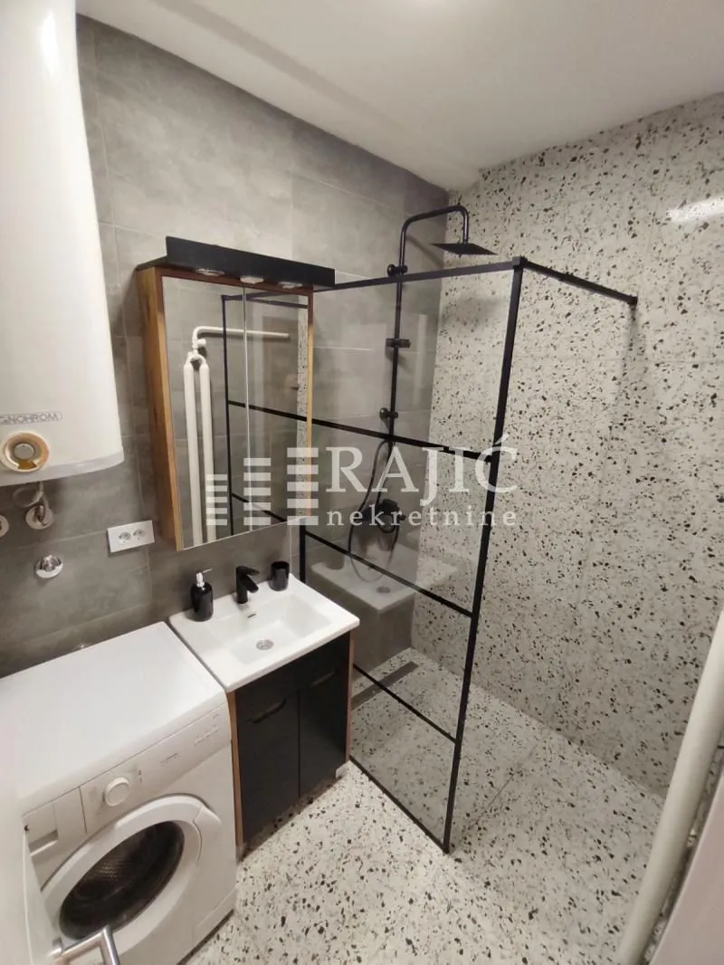 Modern bathroom with a walk-in shower, washbasin, and washing machine.