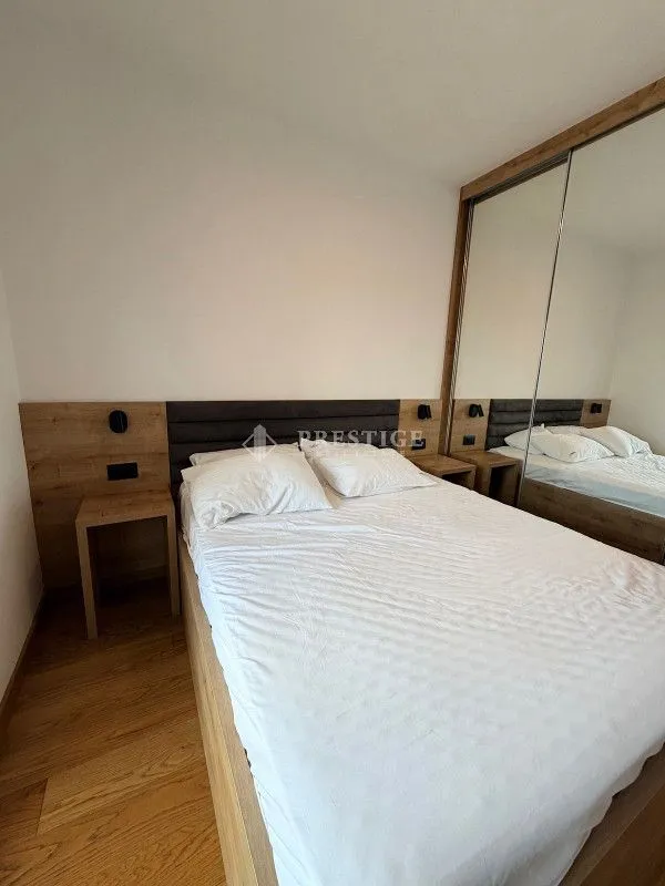 Spavaća soba sa bračnim krevetom, drvenim noćnim stočićima i velikim ugradnim garderoberom sa ogledalom.