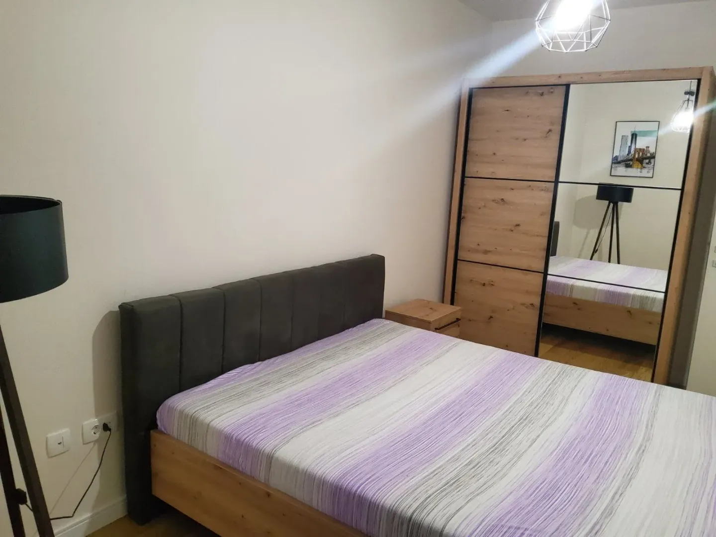 Furnished bedroom with a double bed and a large mirrored wardrobe.