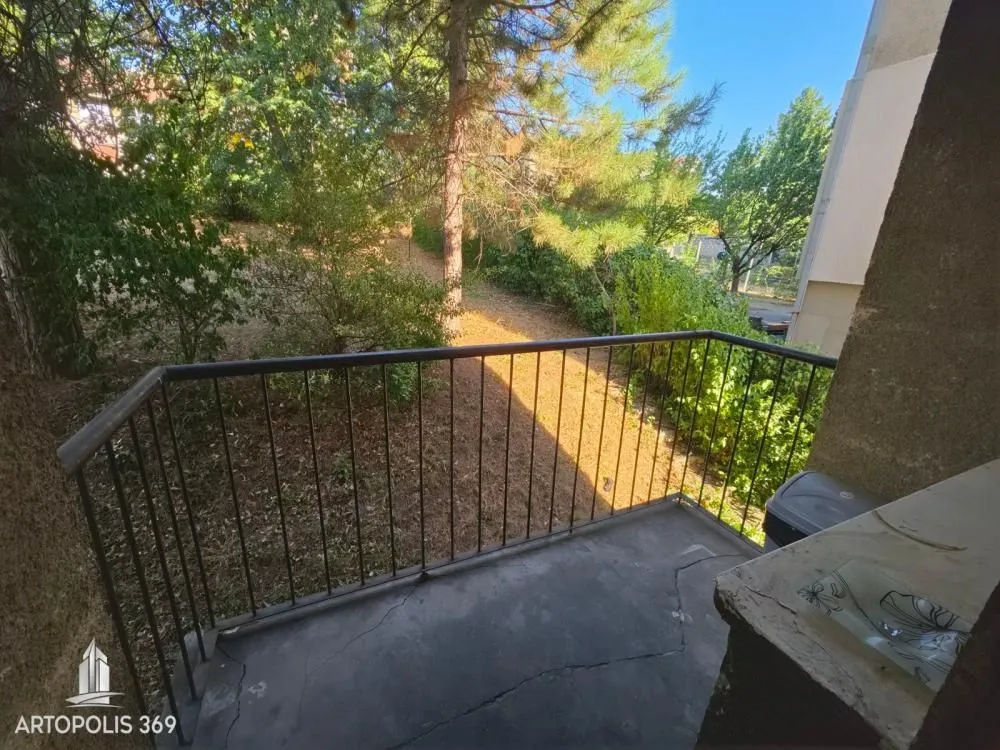 Balkon sa metalnom ogradom i pogledom na zelenilo i drveće.