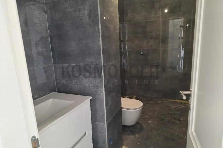 Pogled na kupatilo sa tamnim pločicama i sanitarijama u ugradnji.