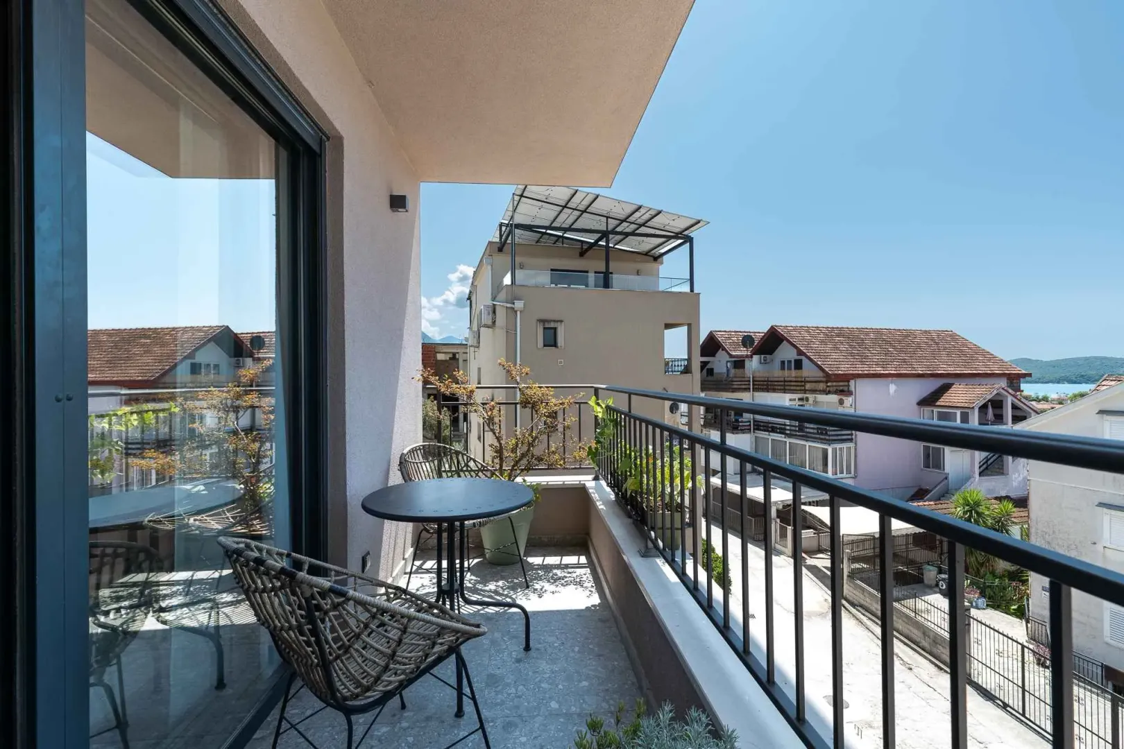 Namješten balkon sa garniturom za sjedenje i pogledom na okolne zgrade i naselje.
