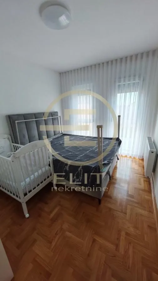 Spavaća soba sa bračnim krevetom, krevetcem za bebe i parketom na podu.
