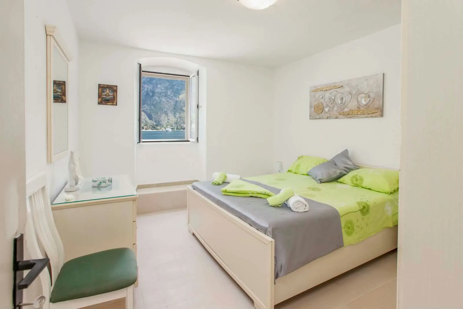 Bright bedroom with a double bed, dresser, and a sea view through the window.