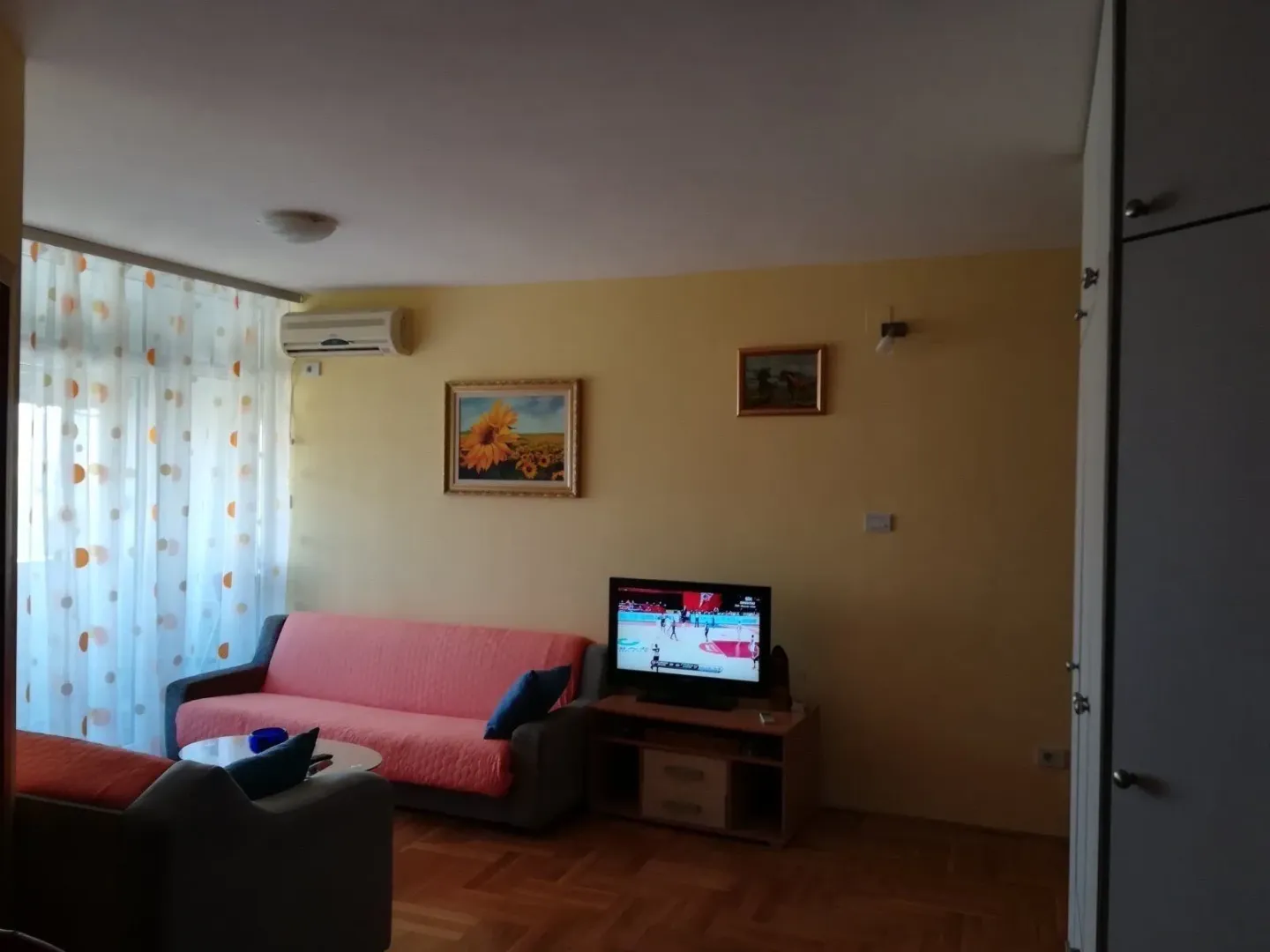 Living room with a pink sofa, TV, and parquet flooring.