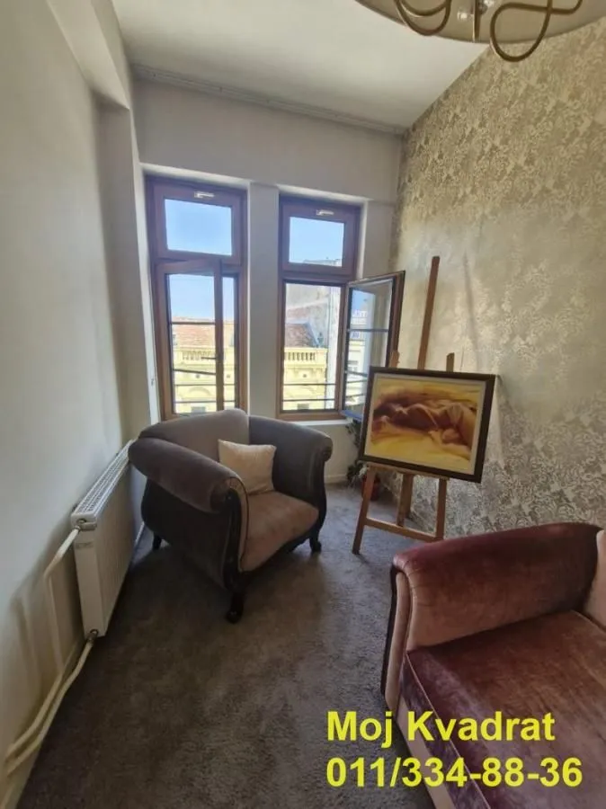 Small living room with armchairs, an easel, and two windows.