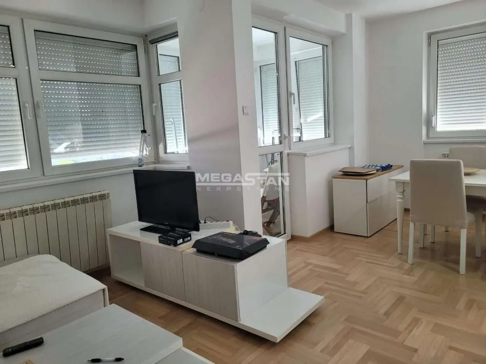 Dnevna soba sa garniturom, televizorom i trpezarijskim stolom pored prozora.