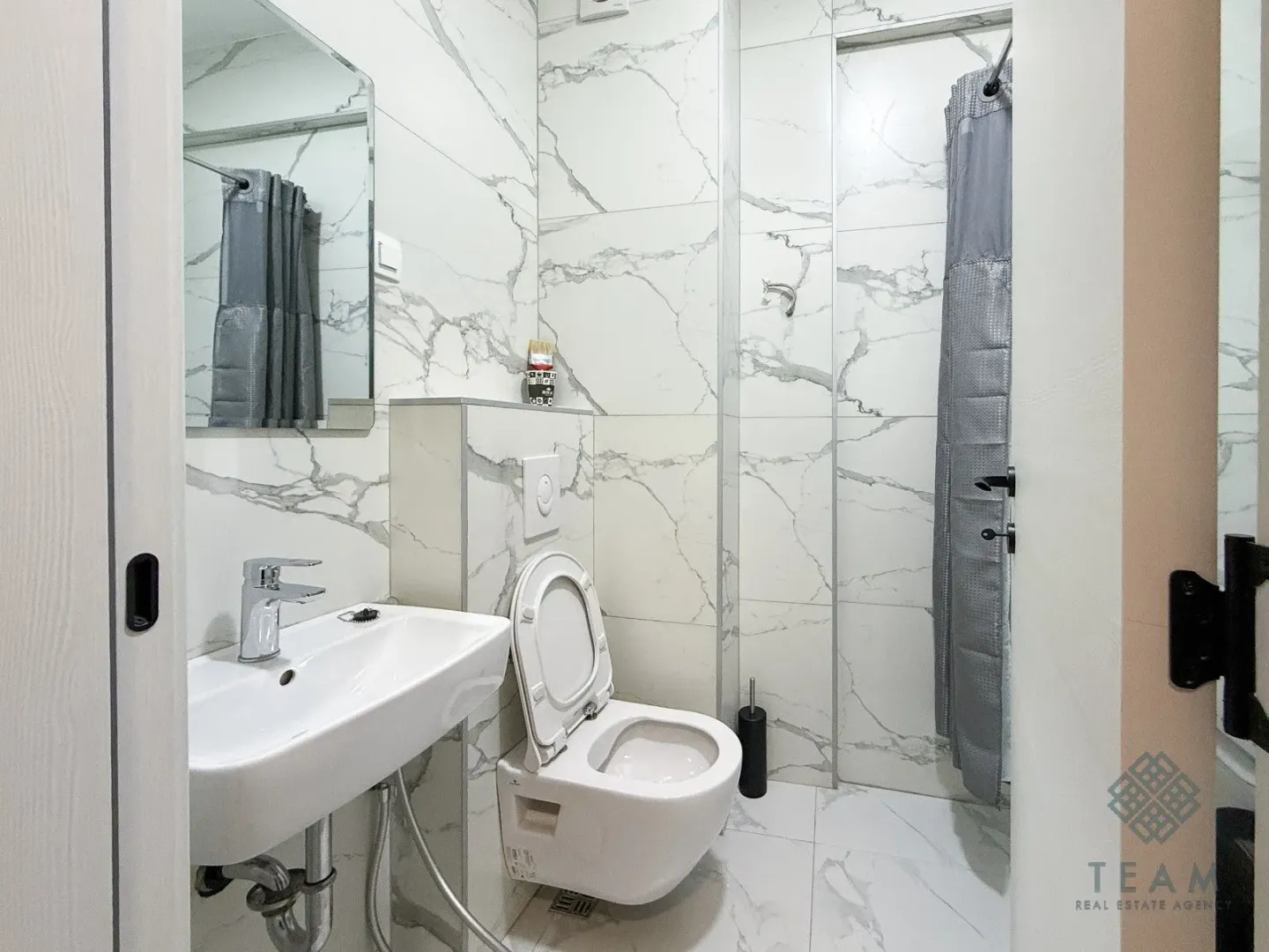 Small bathroom with white marble-effect tiles, a sink, and a walk-in shower.