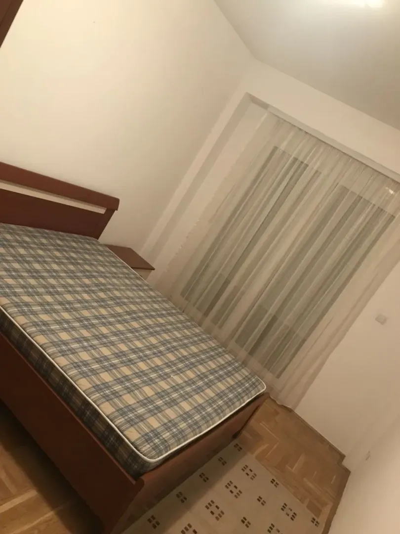 Jednostavno namještena spavaća soba sa bračnim krevetom i prozorom sa zavjesom.