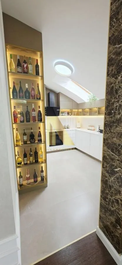 Pogled iz hodnika na moderno uređenu kuhinju sa osvetljenom vinskom vitrinom.