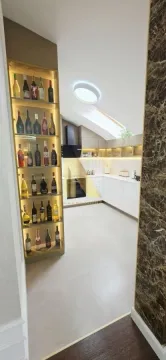 Pogled iz hodnika na moderno uređenu kuhinju sa osvetljenom vinskom vitrinom. - image 7